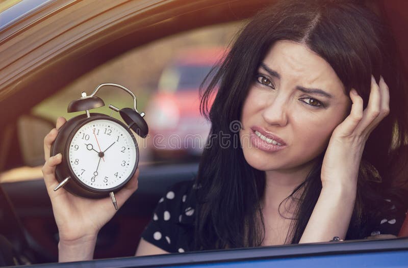Worried woman sitting inside her car showing alarm clock running late to work. Worried woman sitting inside her car showing alarm clock running late to work