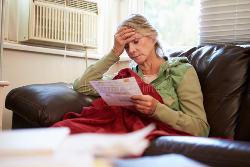 Worried Senior Woman Sitting On Sofa Looking At Bills With Hand On Head. Worried Senior Woman Sitting On Sofa Looking At Bills With Hand On Head