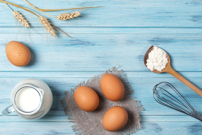 Bestandteile für das Kochen, Milch, Eier, Weizenmehl und Küchengeschirr auf blauem hölzernem Hintergrund, Draufsicht lizenzfreie stockbilder Bestandteile für das Kochen, Milch, Eier, Weizenmehl und Küchengeschirr auf blauem hölzernem Hintergrund, Draufsicht lizenzfreie stockbilder