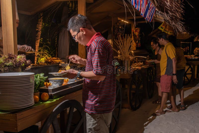 Besucher, die Nahrung während des internationalen Kücheabendessens draußen gegründet am Inselrestaurant nehmen lizenzfreie stockfotografie Besucher, die Nahrung während des internationalen Kücheabendessens draußen gegründet am Inselrestaurant nehmen lizenzfreie stockfotografie