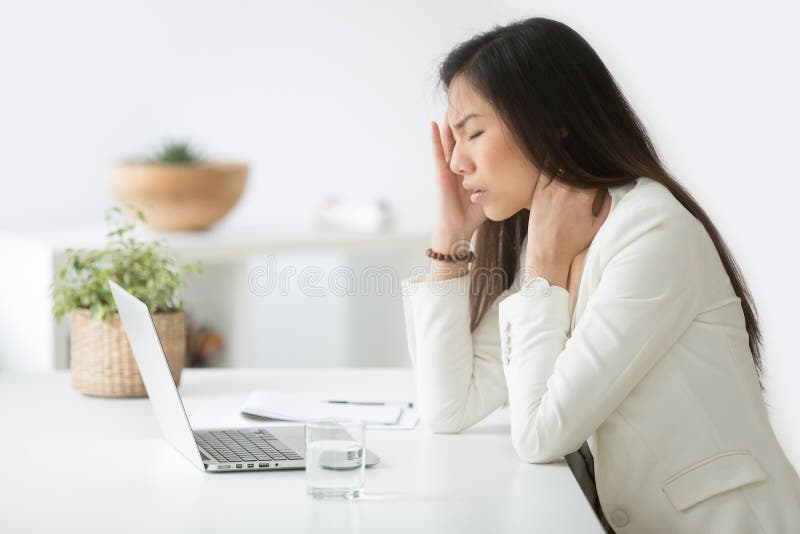 Betonte asiatische Geschäftsfrau, die Kopfschmerzen oder Migräne bei der Arbeit hat