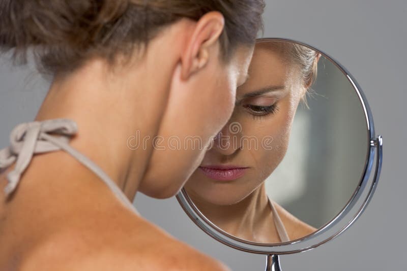 Betonte junge Frau, die im Spiegel schaut