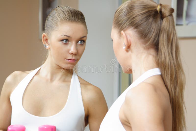 Beutiful blonde girl looking in mirror fitness gym