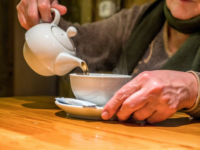 Bevanda di versamento della teiera di vista del primo piano nella tazza in mani senior immagine stock Bevanda di versamento della teiera di vista del primo piano nella tazza in mani senior immagine stock