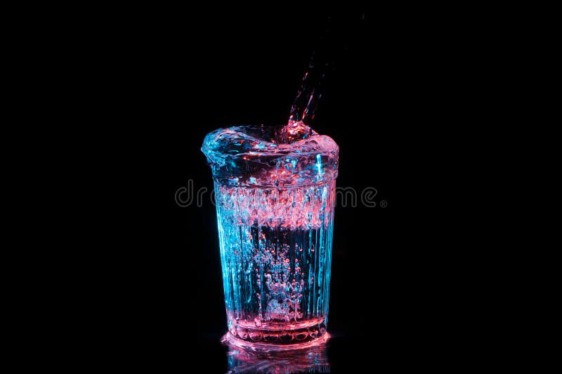 Bevanda pura che è versata in un vetro d'annata nell'ambito delle luci rosse e blu isolate su un fondo nero. Bevanda pura che è versata in un vetro d'annata con le creste e traboccando nell'ambito delle luci rosse e blu isolate su un fondo nero