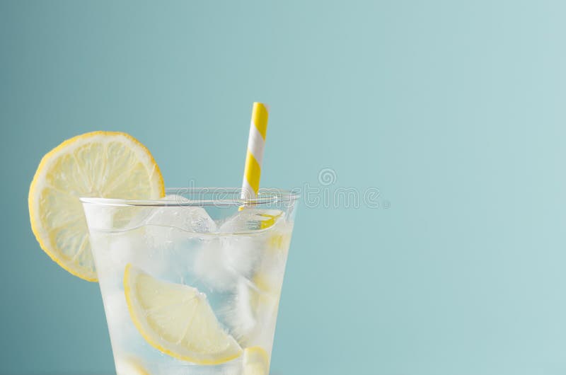 Bevanda rinfrescante a luce fredda per feste con fette di limone, cubetti di ghiaccio, paglia tonica e gialla in vetro elegante a