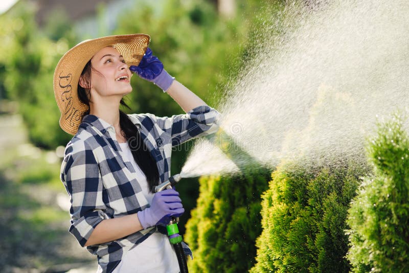 Bewässerungsgarten der schönen jungen Gärtnerfrau am heißen Sommertag lizenzfreie stockfotografie Bewässerungsgarten der schönen jungen Gärtnerfrau am heißen Sommertag lizenzfreie stockfotografie