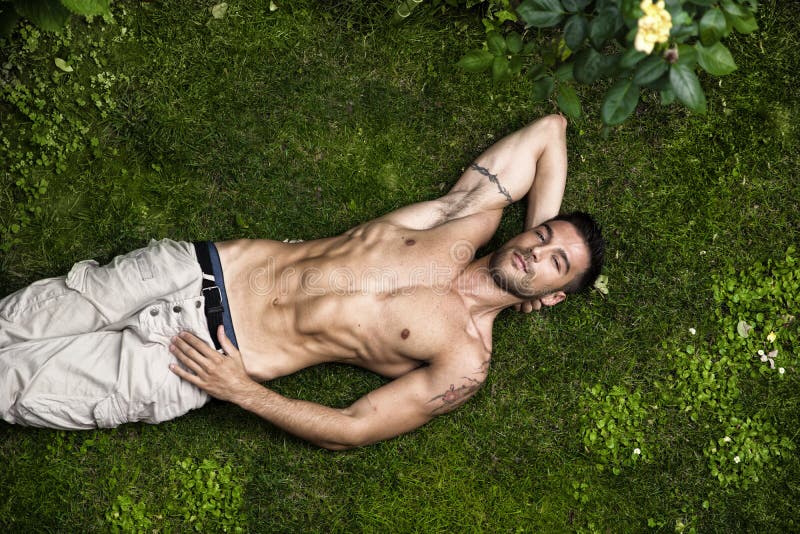 Bez koszuli dysponowanego samiec modela relaksujący lying on the beach na trawie