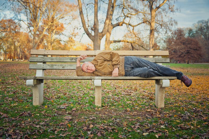 A sad old man outside sleeping on a bench. The image orientation is horizontal and there is copy space. A sad old man outside sleeping on a bench. The image orientation is horizontal and there is copy space.