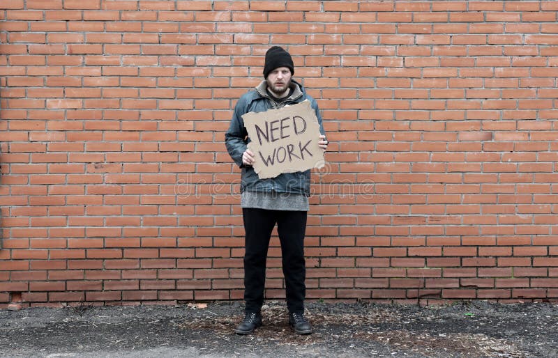 Bezdomny trzyma kawałek kartonu z napisami potrzebuje pracy. uchodźca szuka pracy na murze. samiec w brudzie