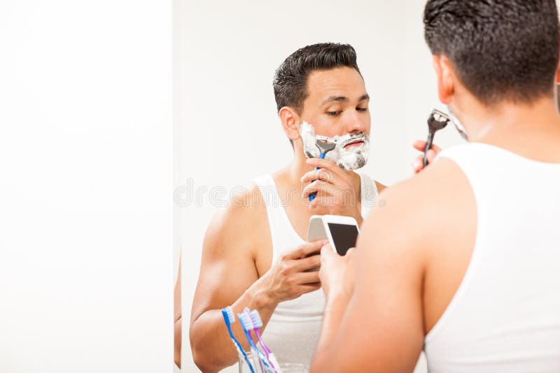 Bezige mens die en in de badkamers scheren texting stock foto Bezige mens die en in de badkamers scheren texting stock foto