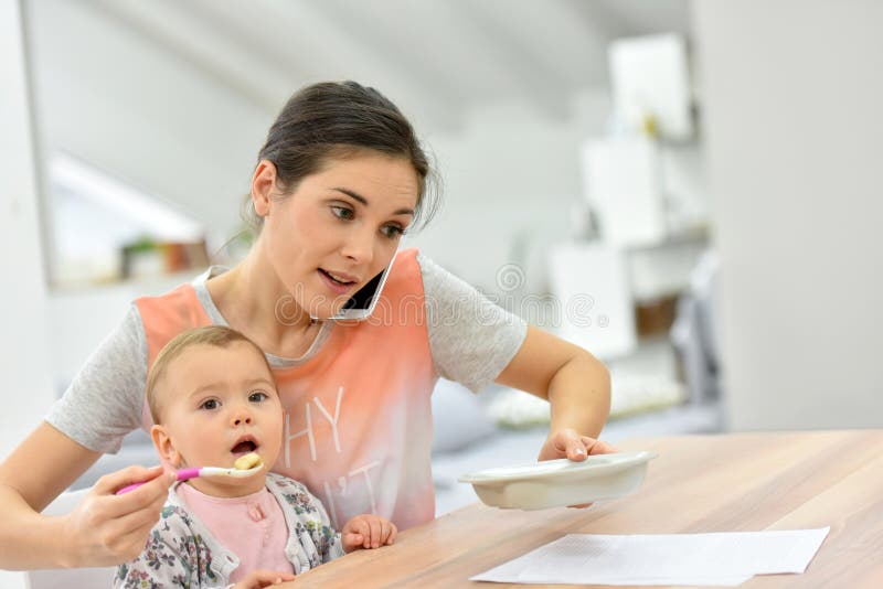 Bezige moeder voedende baby en het spreken op de telefoon stock fotografie Bezige moeder voedende baby en het spreken op de telefoon stock fotografie