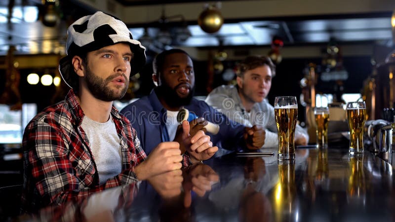 Bezorgde multiraciale mannelijke vrienden die op gelijke in bar letten, die voor teamdoel toejuichen stock foto's Bezorgde multiraciale mannelijke vrienden die op gelijke in bar letten, die voor teamdoel toejuichen stock foto's