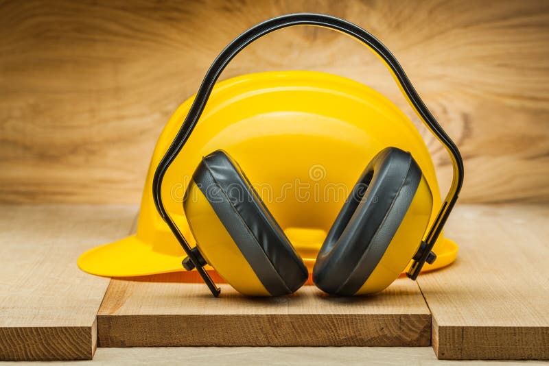 Bezpieczeństwo praca żółty hełm i słuchawki na drewnianych deskach zamykamy w górę fotografia royalty free Bezpieczeństwo praca żółty hełm i słuchawki na drewnianych deskach zamykamy w górę fotografia royalty free