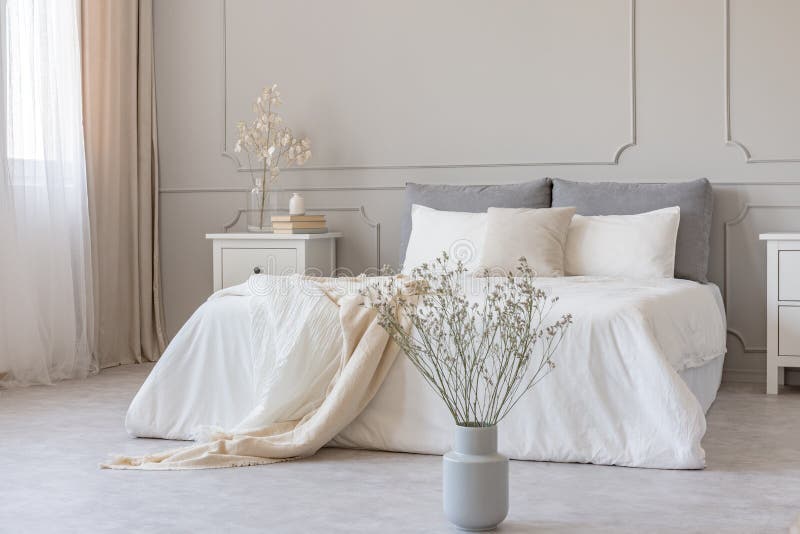 Biali kwiaty w wazie w eleganckim popielatym sypialni wnętrzu z prostą pościelą