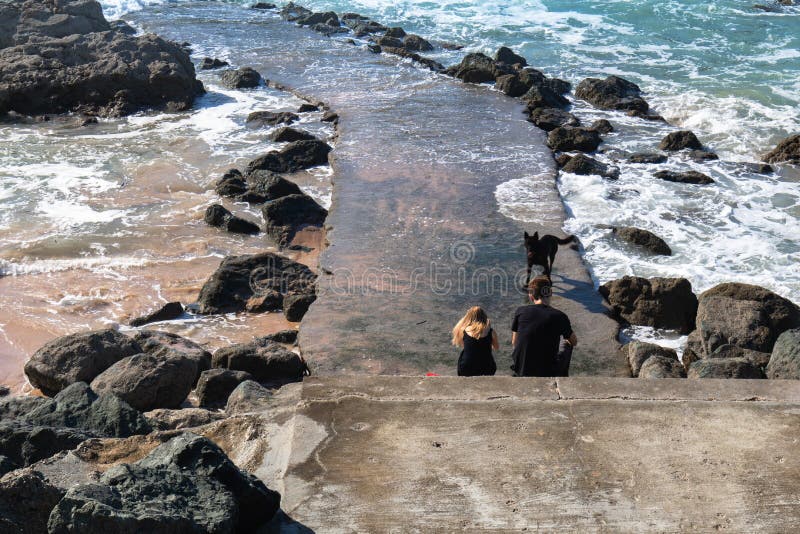 Biarritz, França - 13 de setembro de 2018: pares que sentam-se no quebra-mar do passadiço com um cão que aprecia a vista bonita e fotos de stock Biarritz, França - 13 de setembro de 2018: pares que sentam-se no quebra-mar do passadiço com um cão que aprecia a vista bonita e fotos de stock