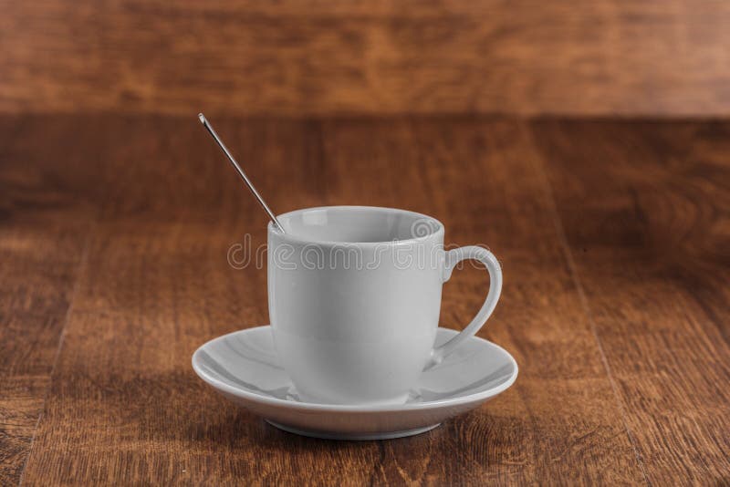 Biała coffe filiżanka z łyżką na białym spodeczku na ciemnego brązu drewnianym tle obrazy stock Biała coffe filiżanka z łyżką na białym spodeczku na ciemnego brązu drewnianym tle obrazy stock