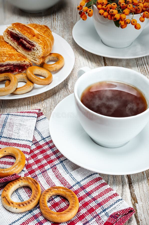 Biała herbaciana filiżanka na rocznika drewnianym stole z bagels i croissant obraz royalty free Biała herbaciana filiżanka na rocznika drewnianym stole z bagels i croissant obraz royalty free