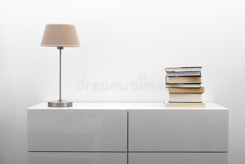 Biała komódka z lampą i książkami w jaskrawym wnętrzu