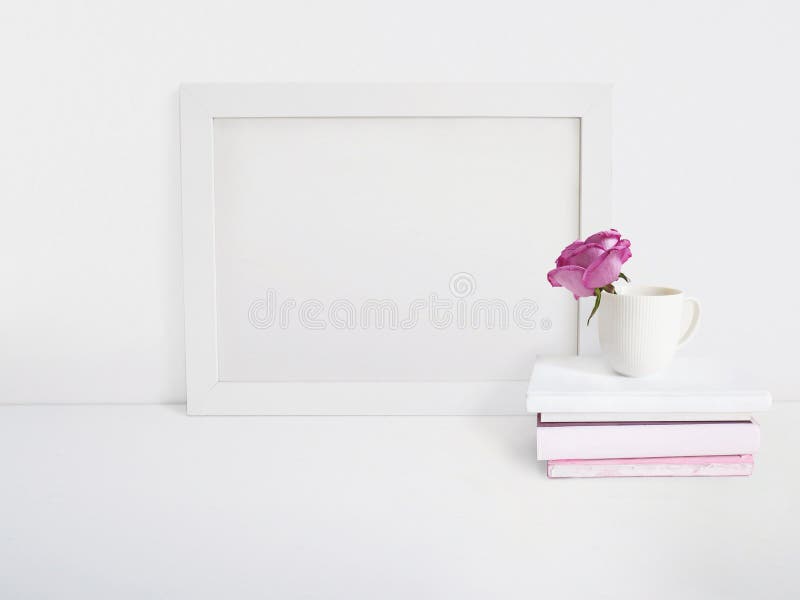Biały pusty drewnianej ramy mockup z róża kwiatem w porcelany filiżance stosie książki kłama na stole i plakat zdjęcie stock Biały pusty drewnianej ramy mockup z róża kwiatem w porcelany filiżance stosie książki kłama na stole i plakat zdjęcie stock