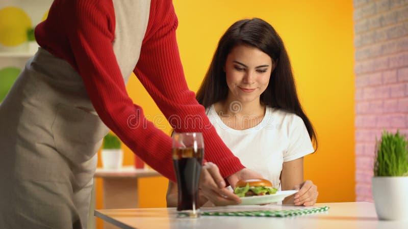 Bibita ed hamburger del servizio del cameriere al cliente femminile, spuntino non sano