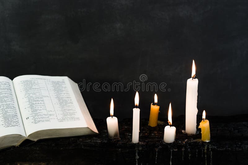 Bible and candle on an old wooden burnt table. Beautiful dark background. Religious concept.