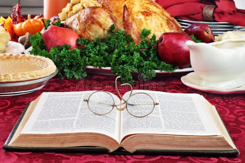 Open Bible with glasses lying on a holiday dinner table with prepared turkey and fixings in background. Open Bible with glasses lying on a holiday dinner table with prepared turkey and fixings in background.