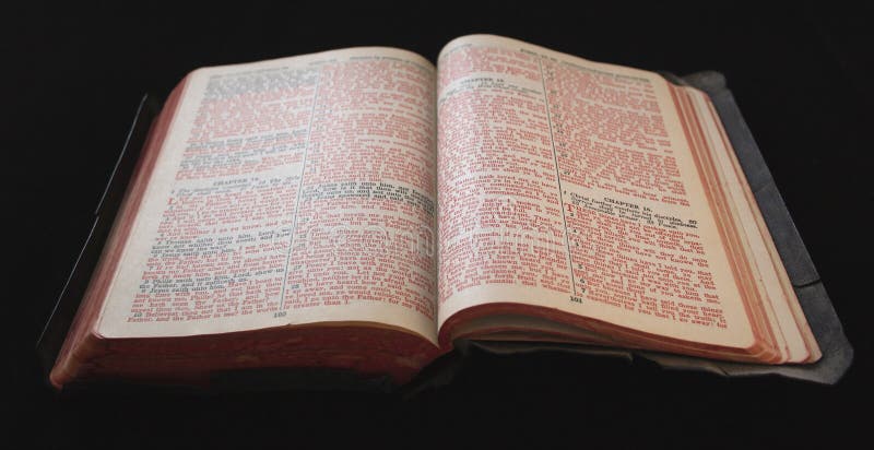 An old bible with tattered edges and red and black text against a black background. An old bible with tattered edges and red and black text against a black background