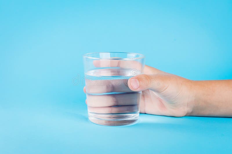 Bicchiere d'acqua a disposizione sul blu fotografia stock libera da diritti Bicchiere d'acqua a disposizione sul blu fotografia stock libera da diritti