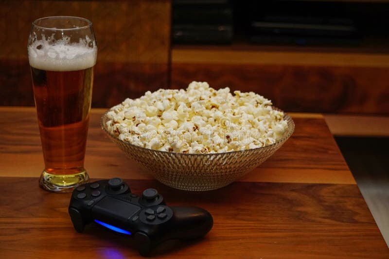 Bicchiere di birra una ciotola di popcorn e un controller di videogioco su un tavolo di legno fotografia stock