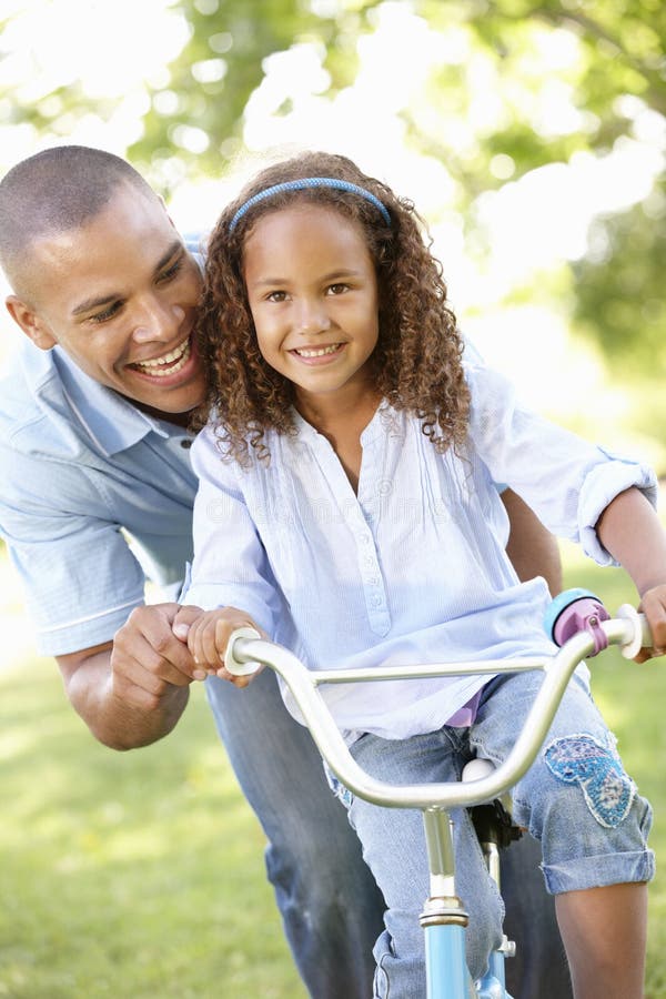 Bici del paseo de Teaching Daughter To del padre en parque imagen de archivo Bici del paseo de Teaching Daughter To del padre en parque imagen de archivo