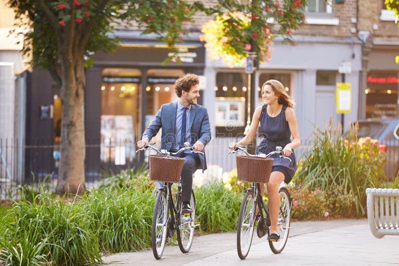 Bici di And Businessman Riding della donna di affari attraverso il parco della città