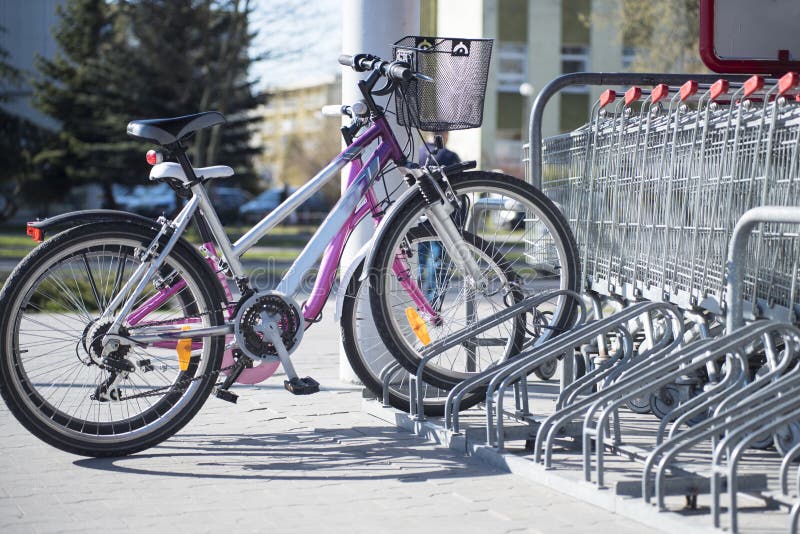 Parked bikes in a parking rack in front of supermarket with visible store carts parked in a row. One men's bike and the other woman's. Parked bikes in a parking rack in front of supermarket with visible store carts parked in a row. One men's bike and the other woman's.