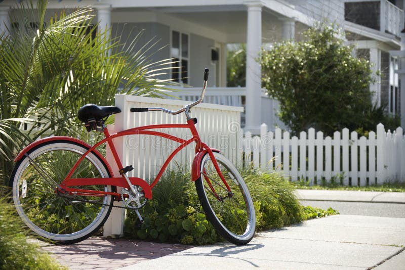 Red beach cruiser bicycle propped against fence in front of house. Red beach cruiser bicycle propped against fence in front of house.