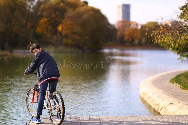 Bicyclette de tour de garçon d'adolescent sur le landscapce de chute de fond de lac de parc de ville image libre de droits Bicyclette de tour de garçon d'adolescent sur le landscapce de chute de fond de lac de parc de ville image libre de droits