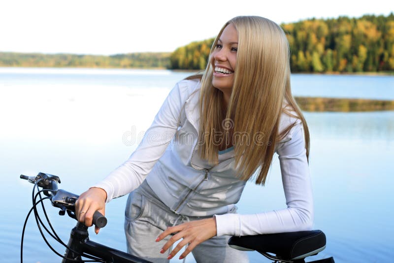 Young smiling woman holds the bicycle at still blue lake. Young smiling woman holds the bicycle at still blue lake