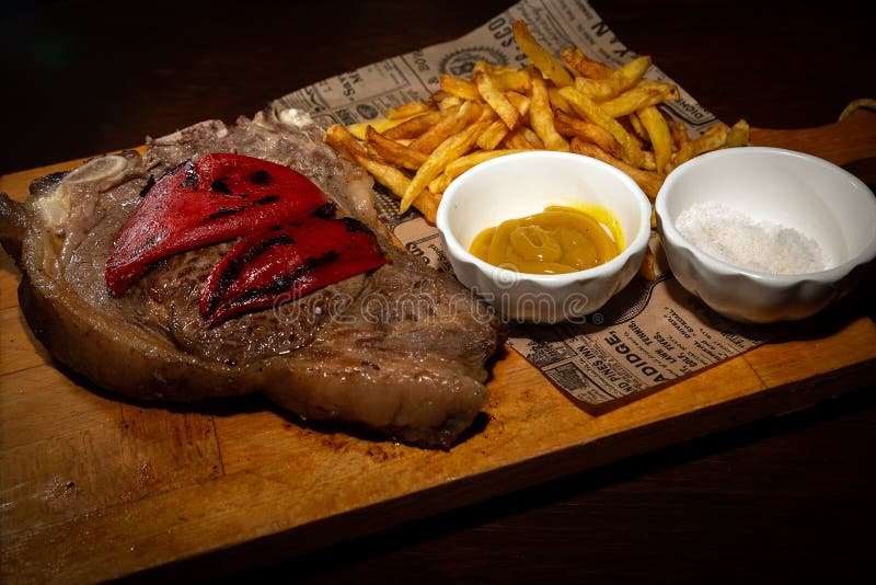 Bife raro grelhado servido na placa de madeira com batatas fritadas imagem de stock Bife raro grelhado servido na placa de madeira com batatas fritadas imagem de stock