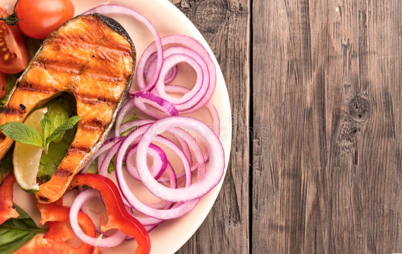 Bife salmon grelhado com cebola e os tomates cortados na esquerda imagem de stock Bife salmon grelhado com cebola e os tomates cortados na esquerda imagem de stock