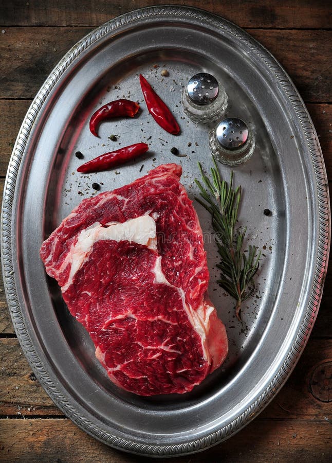 Bifteck de boeuf juteux cru avec le romarin, le sel, le poivre et le poivre de piment d'un plat de fer sur la table en bois images libres de droits Bifteck de boeuf juteux cru avec le romarin, le sel, le poivre et le poivre de piment d'un plat de fer sur la table en bois images libres de droits