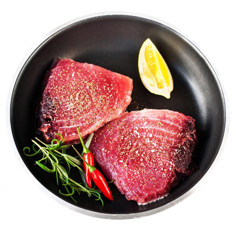 Tuna steak - Raw fresh tuna fillet with herbs, salt and lemon in a frying pan, isolated on white background. Tuna steak - Raw fresh tuna fillet with herbs, salt and lemon in a frying pan, isolated on white background.