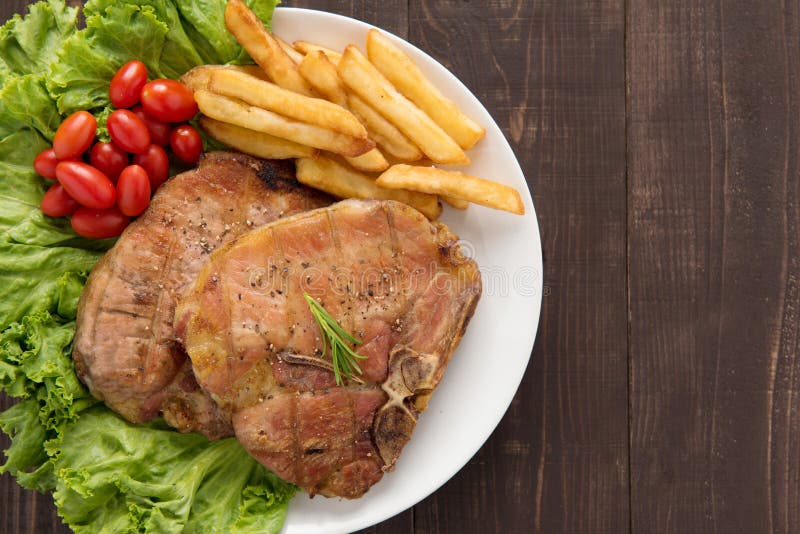 Bifteck et légumes grillés de côtelette de porc avec des pommes frites sur le bois photographie stock libre de droits Bifteck et légumes grillés de côtelette de porc avec des pommes frites sur le bois photographie stock libre de droits