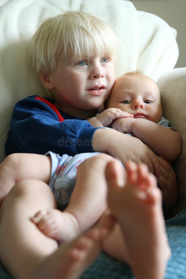 A toddler aged big brother his hugging his little baby sister as the cuddle on the living room couch watching a movie. A toddler aged big brother his hugging his little baby sister as the cuddle on the living room couch watching a movie.