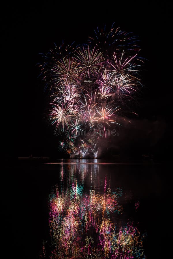 Big crackling explosion in rich fireworks over Brno`s Dam with lake reflection