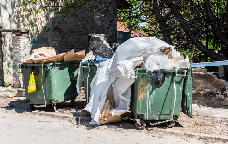 Big two metal dumpster garbage cans full of overflow litter and junk  polluting the street in the city Stock Photo
