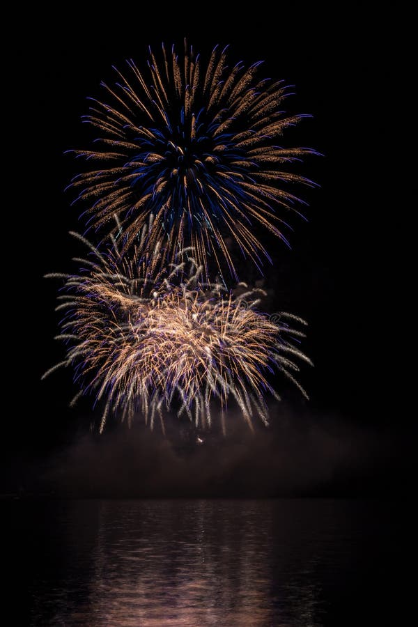 Big gold and blue stars from fireworks over Brno`s Dam with lake reflection