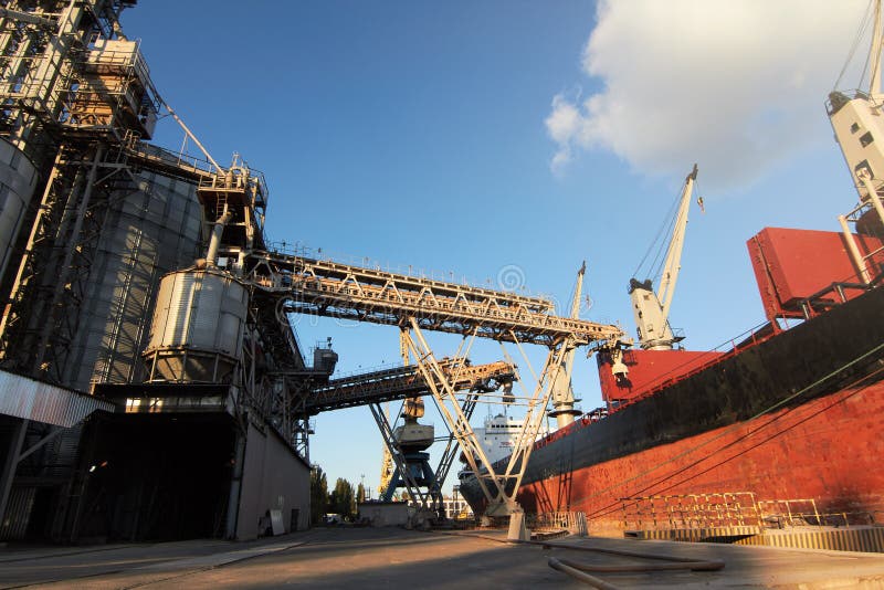 Big grain terminal at seaport. Cereals bulk transshipment from road transport to vessel. Loading grain crops on ship