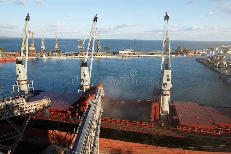 Big grain terminal at seaport. Cereals bulk transshipment from road transport to vessel. Loading grain crops on bulk