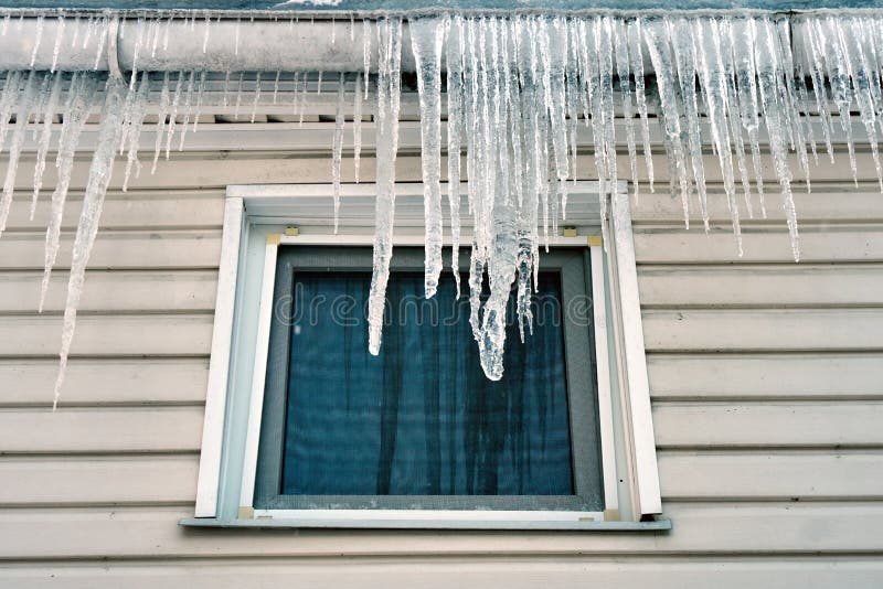 Big icicles hanging on the roof above a window of a cottage in winter or spring