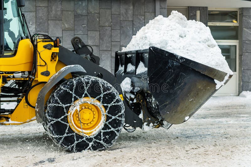 Big loader machine with steel metal chains removing big snow pile from city street at alpine mountain region in winter. Heavy royalty free stock photography Big loader machine with steel metal chains removing big snow pile from city street at alpine mountain region in winter. Heavy royalty free stock photography