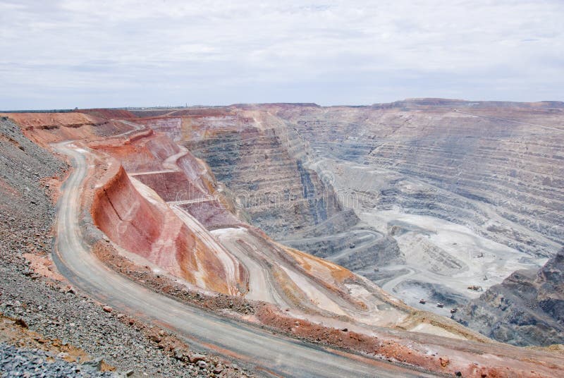 Big mine pit with little dump trucks and reddish soil royalty free stock photos